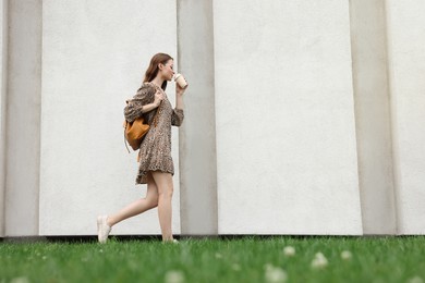 Photo of Young woman with cup of drink walking near stone wall outdoors, space for text