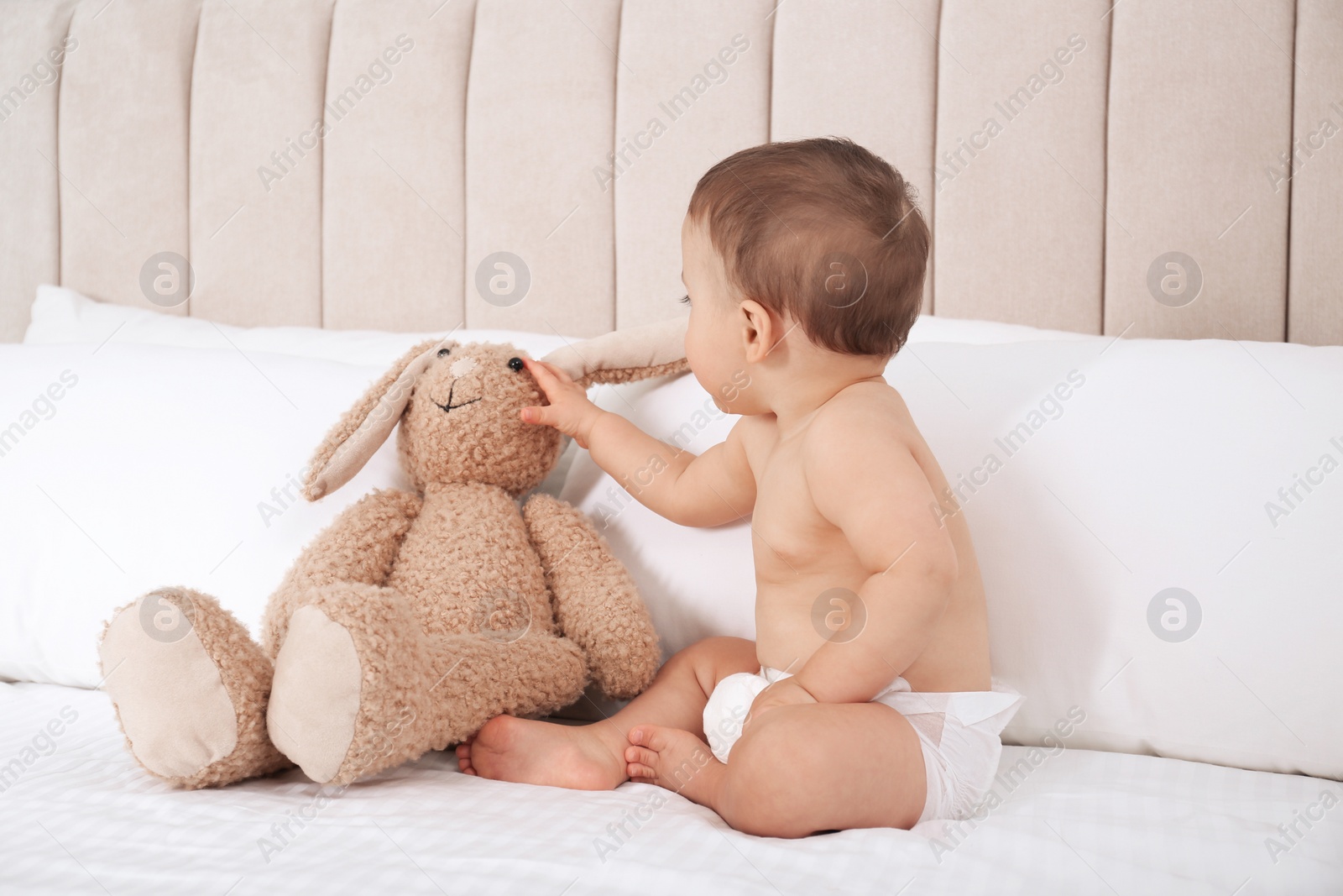 Photo of Cute baby in dry soft diaper with toy bunny on white bed at home