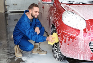 Young worker cleaning automobile wheel at car wash