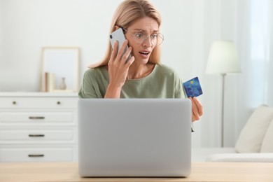 Stressed woman with credit card talking on smartphone at home. Be careful - fraud