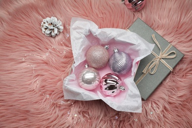Photo of Beautiful Christmas baubles in box on pink faux fur, flat lay