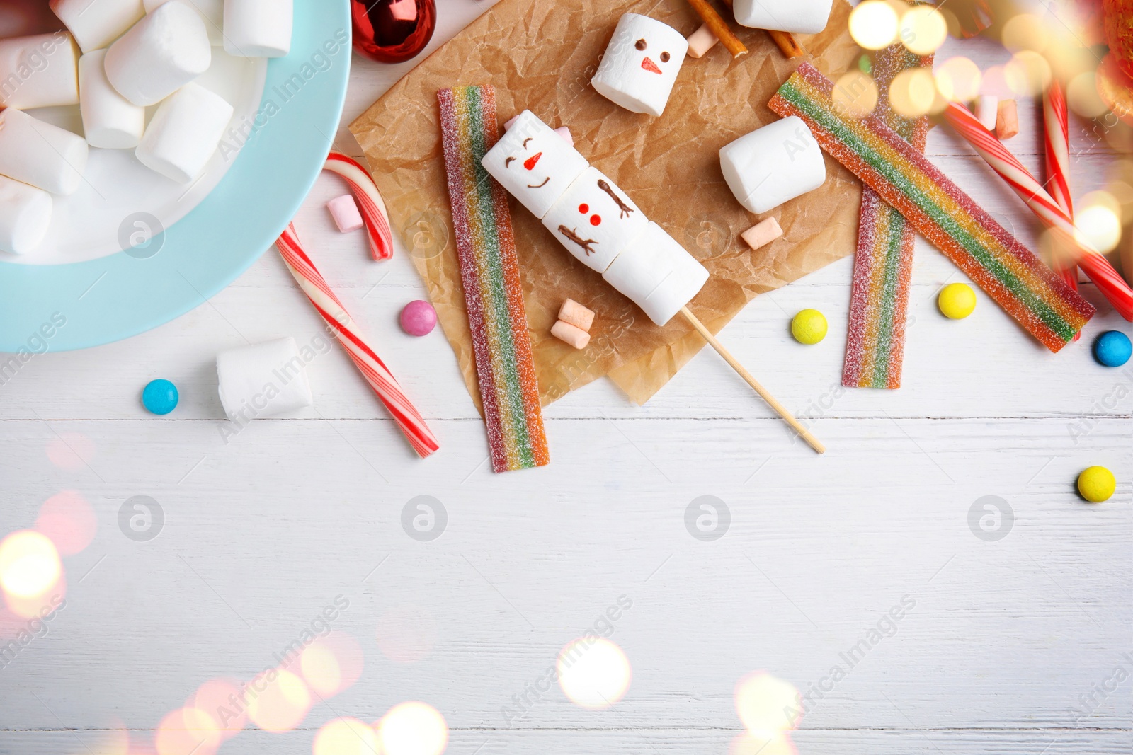 Image of Flat lay composition with funny snowman made of marshmallows on white wooden table, space for text. Bokeh effect 