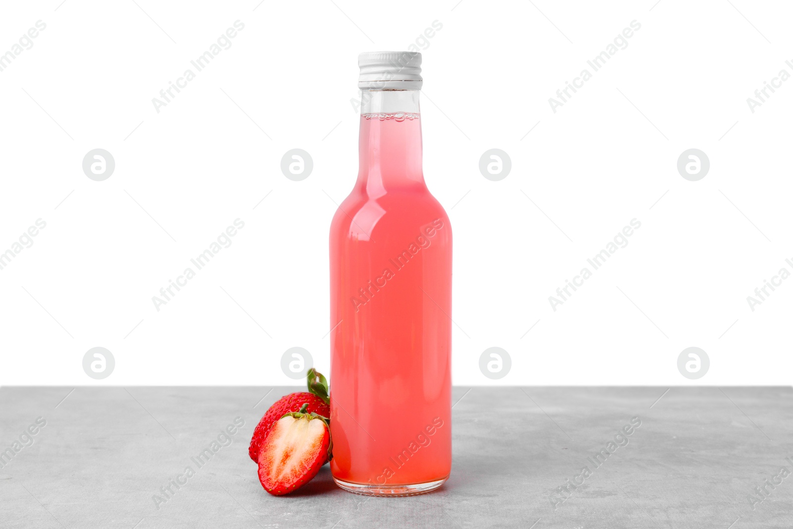 Photo of Delicious kombucha in glass bottle and strawberries on grey table against white background