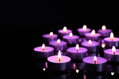 Image of Beautiful burning violet candles on black background. Funeral attributes