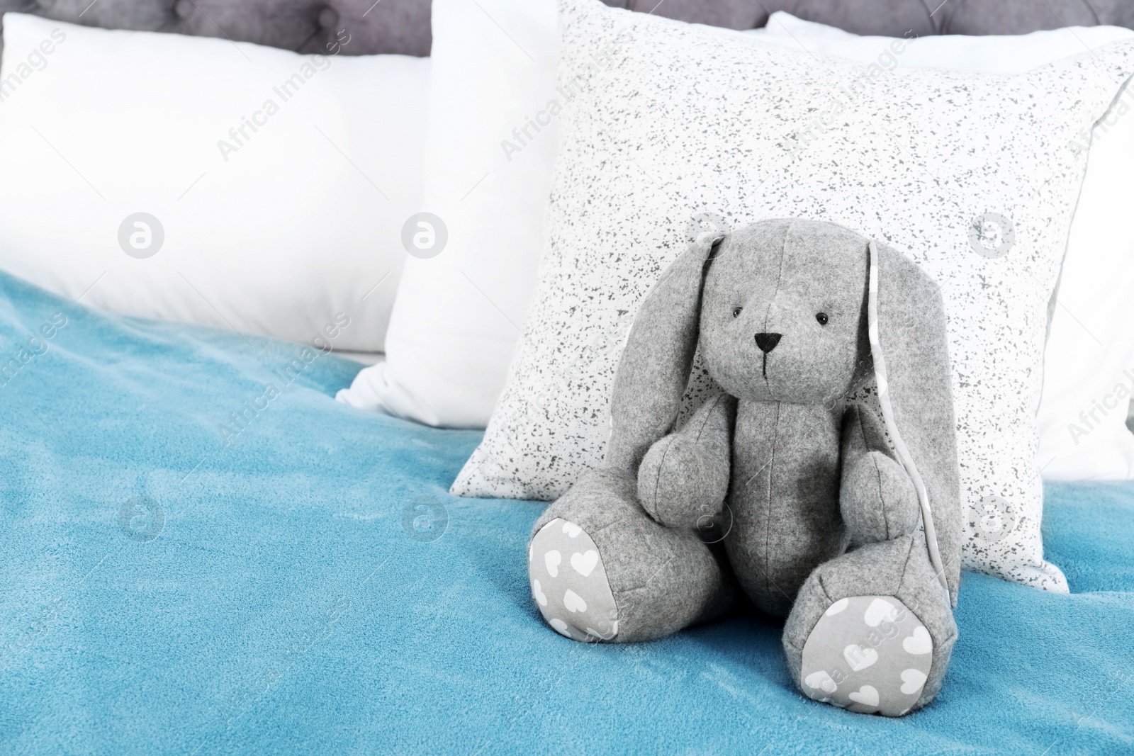 Photo of Cute toy rabbit sitting on bed indoors. Space for text