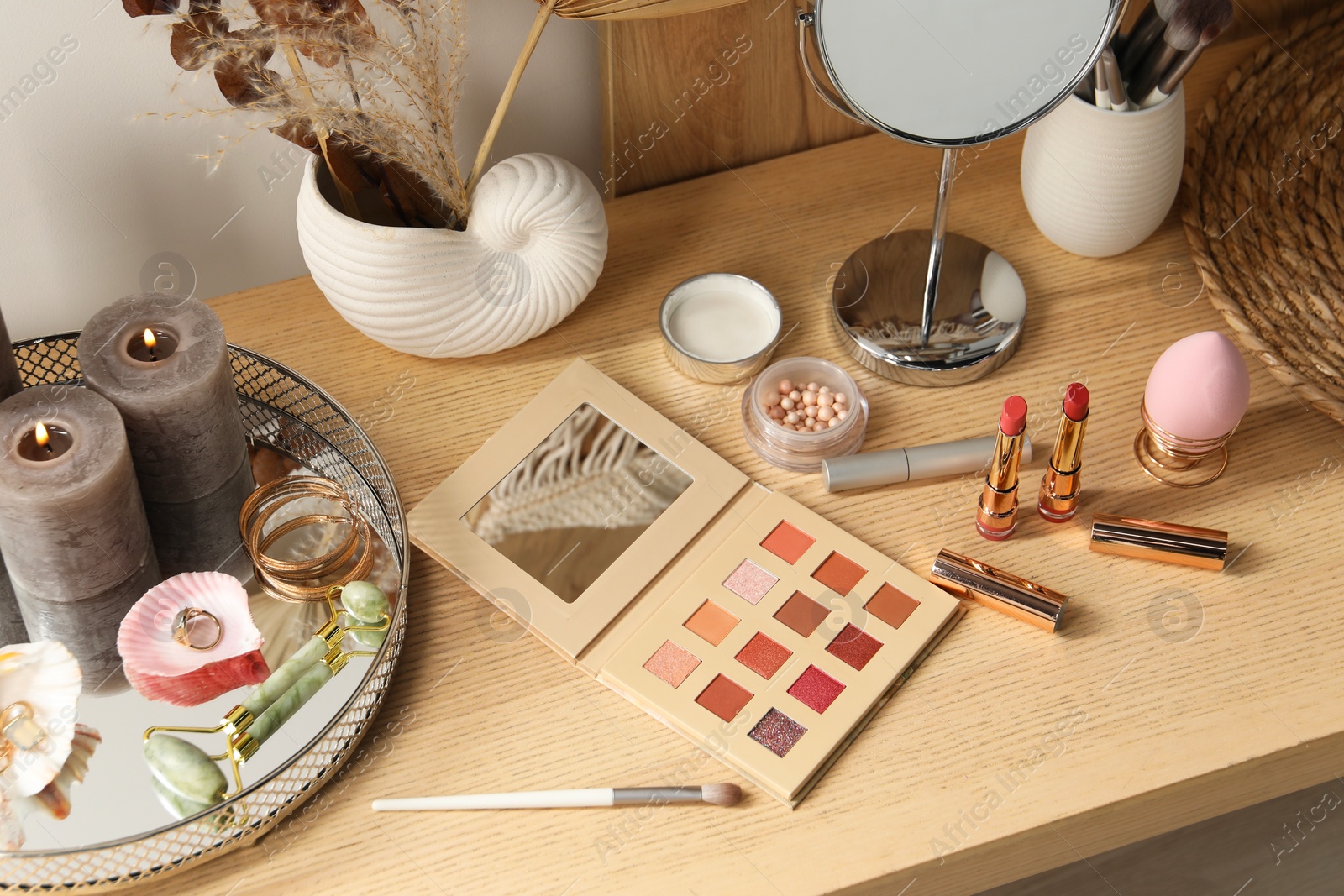 Photo of Burning candles, jewelry and makeup products on wooden dressing table