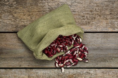 Photo of Overturned sack with dry kidney beans on old wooden table, flat lay