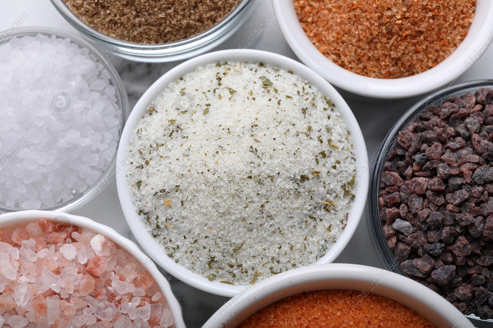 Photo of Different kinds of salt on white table, flat lay