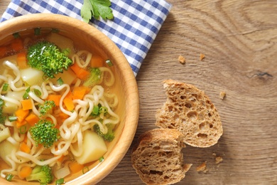 Bowl of fresh homemade vegetable soup on wooden background, flat lay