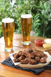 Photo of Tasty roasted chicken wings served with beer on wooden table