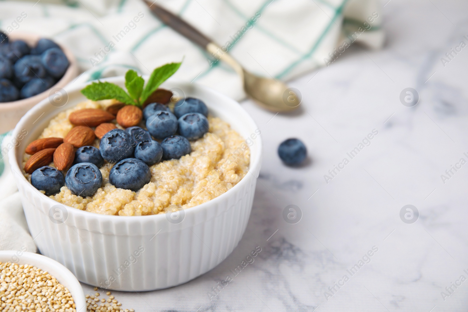 Photo of Bowl of delicious cooked quinoa with almonds and blueberries on white marble table, space for text