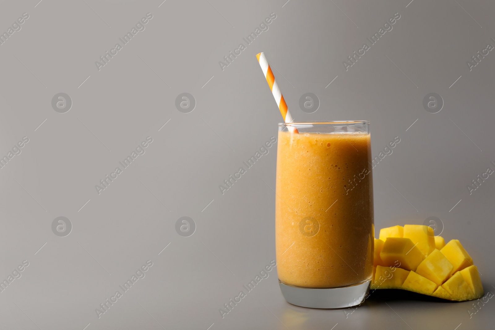 Photo of Glass with delicious fresh fruit smoothie and mango on grey background. Space for text