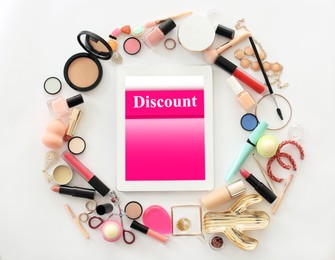 Tablet with word Discount and makeup products on light background, flat lay