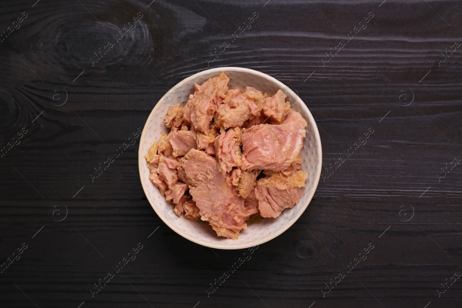 Photo of Bowl with canned tuna on black wooden table, top view