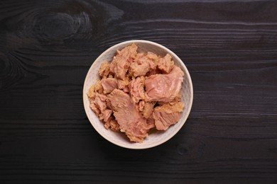 Photo of Bowl with canned tuna on black wooden table, top view