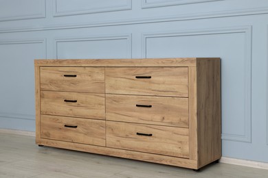 Wooden stylish chest of drawers near grey wall indoors