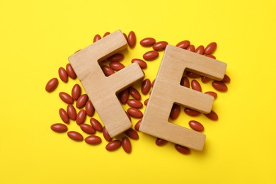 Photo of Wooden letters FE and pills on yellow background, flat lay. Anemia treatment