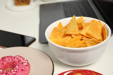 Photo of Bad eating habits at workplace. Tasty tortilla chips in bowl on white table, closeup