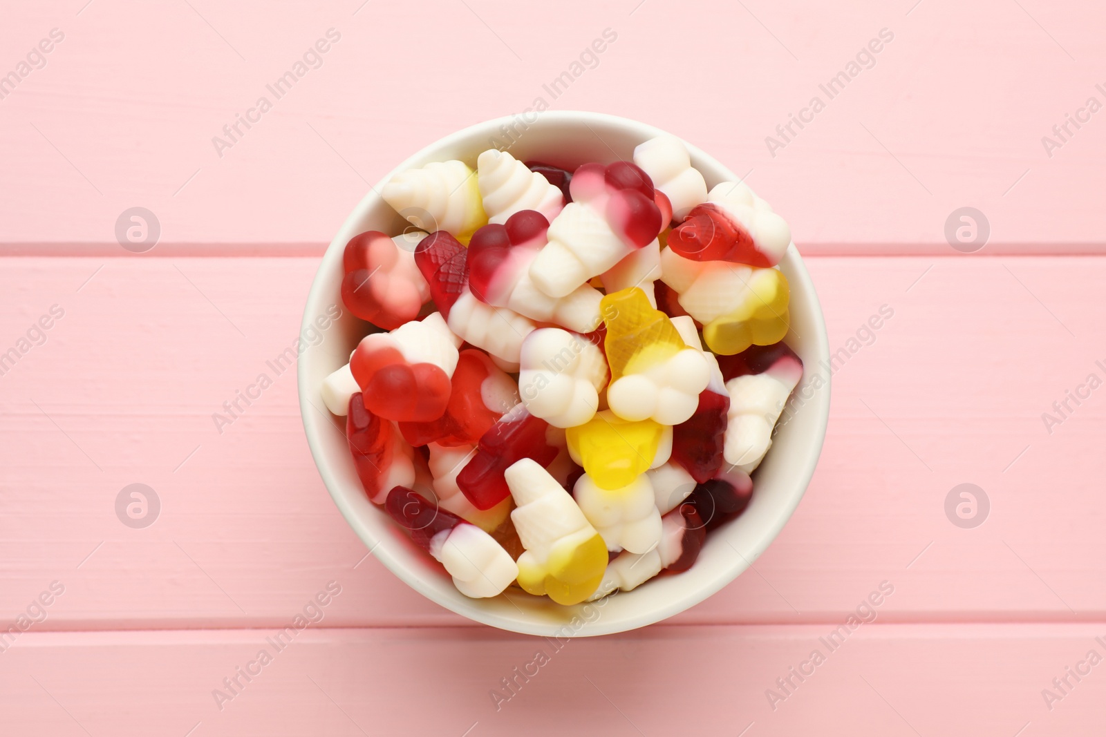 Photo of Delicious gummy ice cream cones shaped candies on pink wooden table, top view