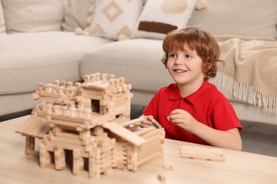 Photo of Cute little boy playing with wooden castle at table in room. Child's toy