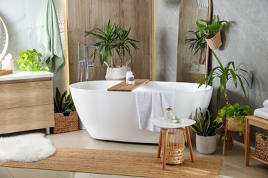 Photo of Modern white tub and beautiful green houseplants in bathroom. Interior design