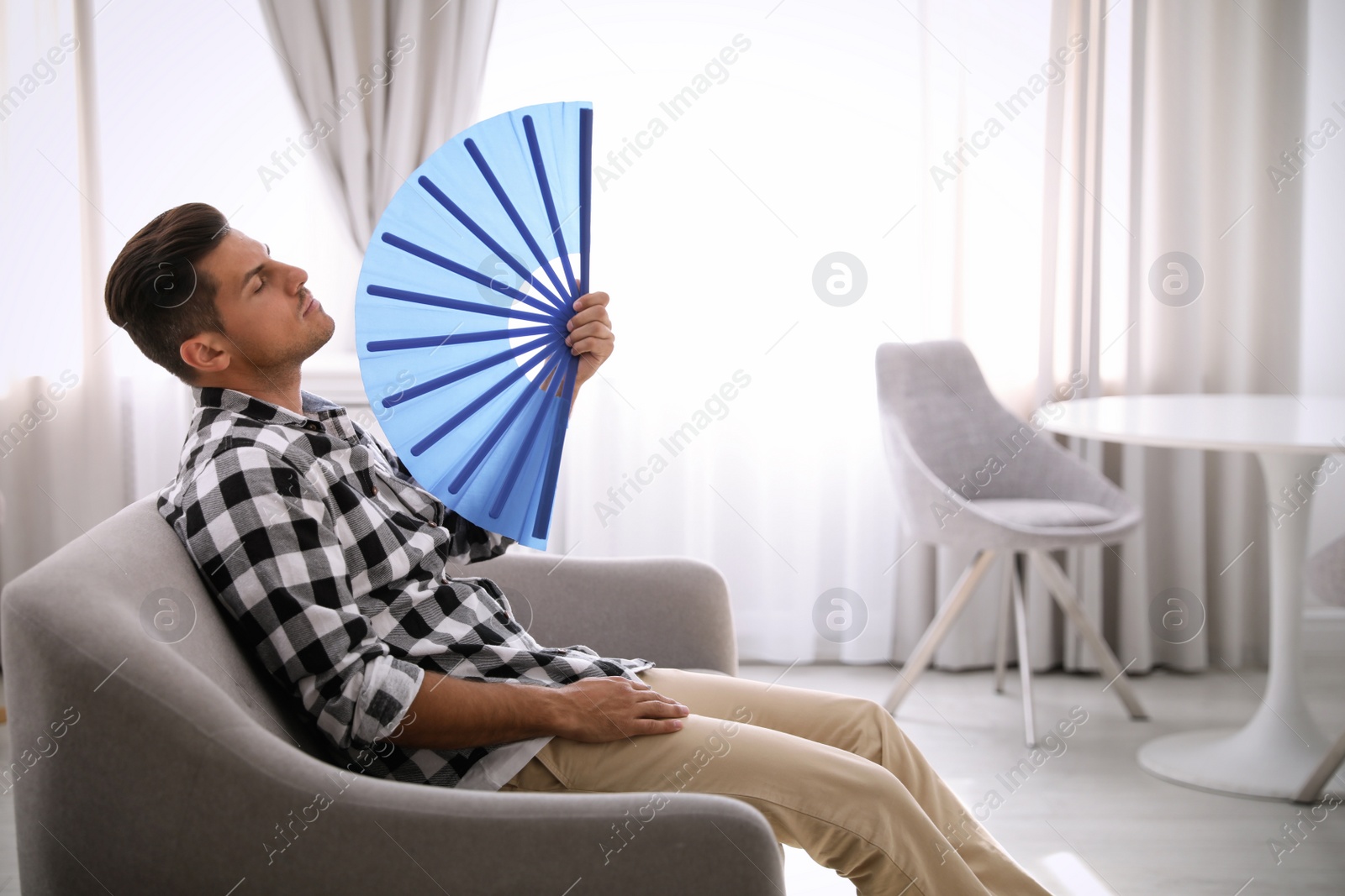 Photo of Man with hand fan sitting on sofa. Summer season