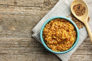 Photo of Fresh whole grain mustard in bowl and dry seeds on wooden table, flat lay. Space for text