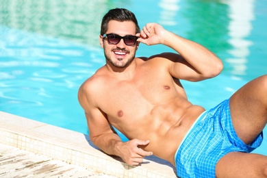 Handsome young man lying near swimming pool on sunny day