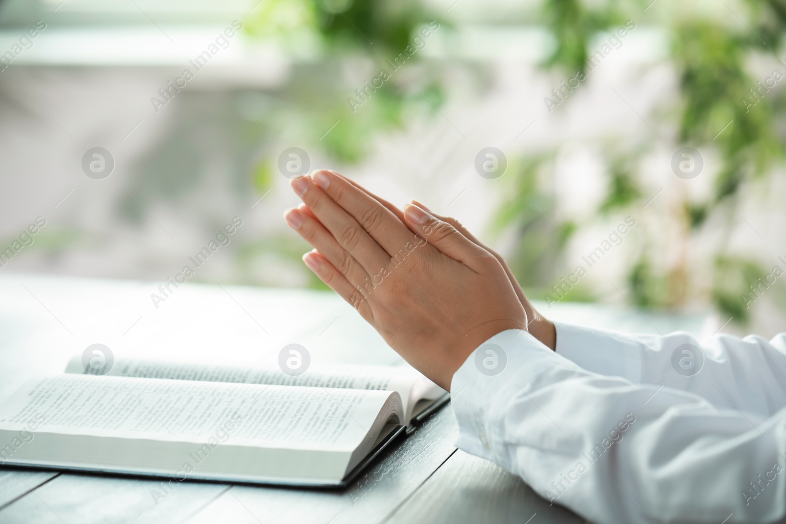 Photo of Woman holding hands clasped while praying at grey wooden table with Bible, closeup