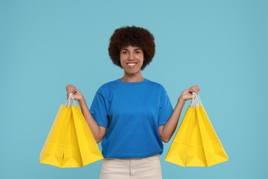 Happy young woman with shopping bags on light blue background