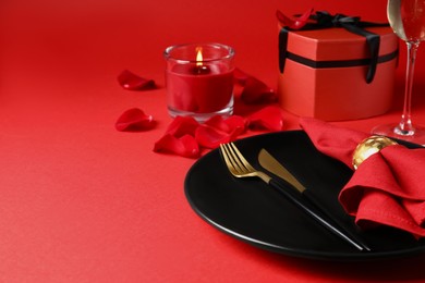 Photo of Beautiful table setting with gift box and burning candle on red table for romantic dinner. Space for text