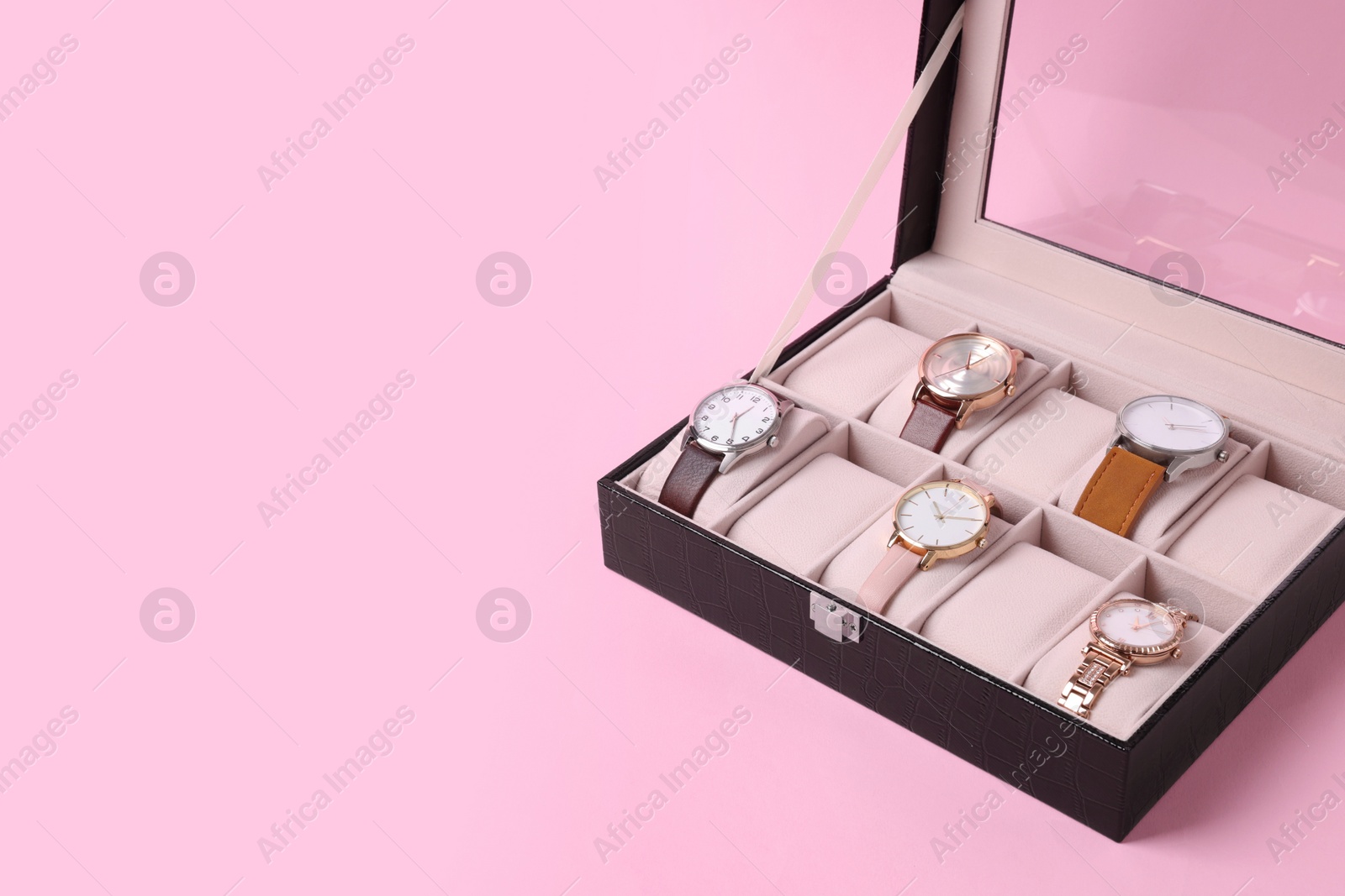 Photo of Black jewelry box with different wristwatches on pink background. Space for text