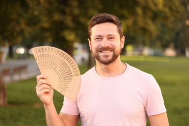 Photo of Happy man holding hand fan in park