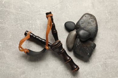 Photo of Black slingshot with stones on light grey table, flat lay