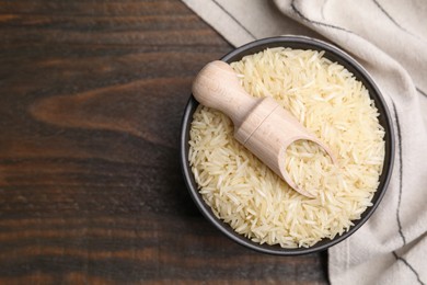 Photo of Bowl and scoop with raw rice on wooden table, top view. Space for text