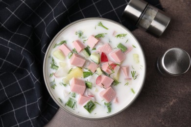 Photo of Delicious cold summer soup (okroshka) with boiled sausage in bowl on brown table, top view