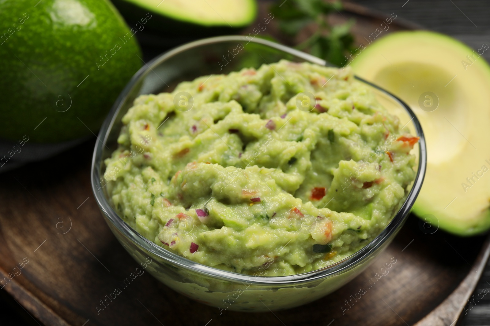 Photo of Delicious guacamole with parsley and fresh avocado on wooden board, closeup