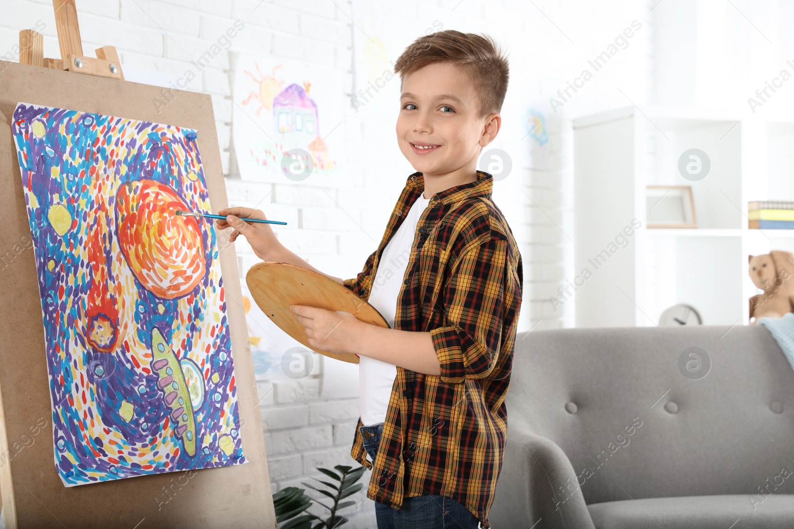 Photo of Cute little child painting on easel at home