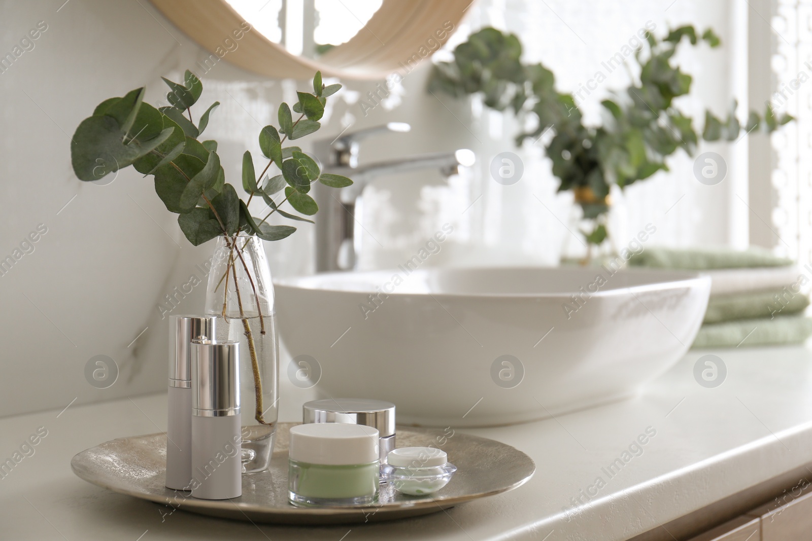 Photo of Fresh eucalyptus branches and cosmetic products on countertop in bathroom