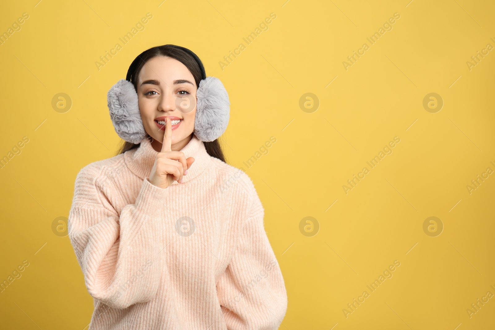 Photo of Beautiful young woman wearing earmuffs on yellow background. Space for text