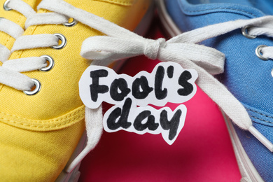 Photo of Shoes tied together and note with phrase FOOL'S DAY on pink background, closeup