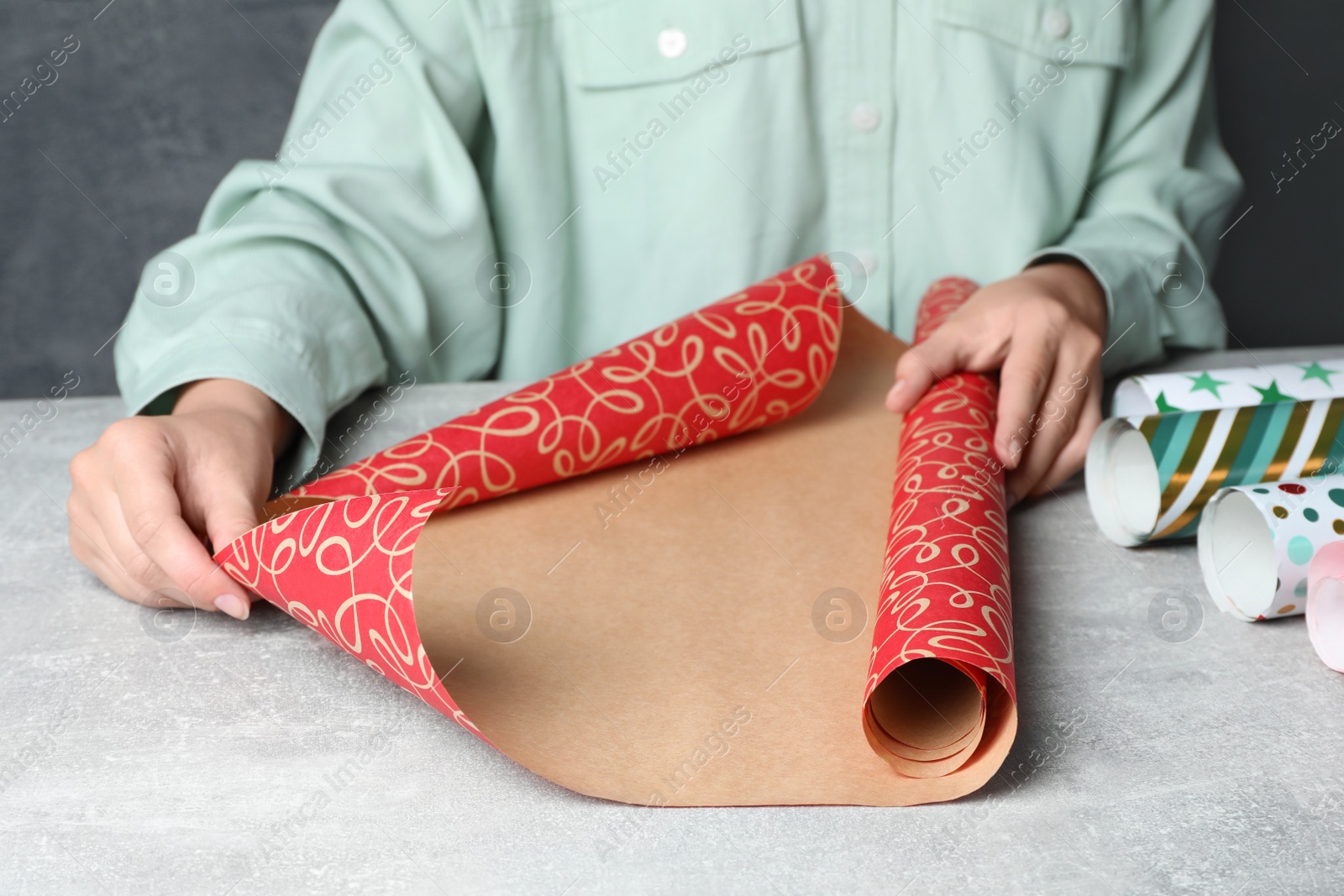 Photo of Woman with roll of beautiful wrapping paper at light grey table, closeup