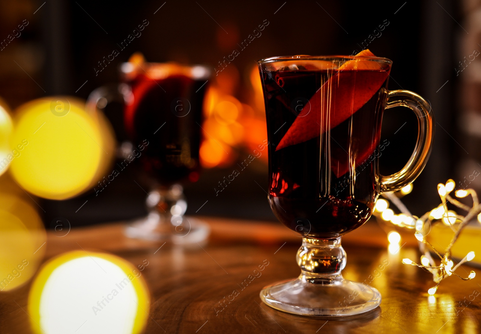 Photo of Tasty mulled wine, festive lights and blurred fireplace on background