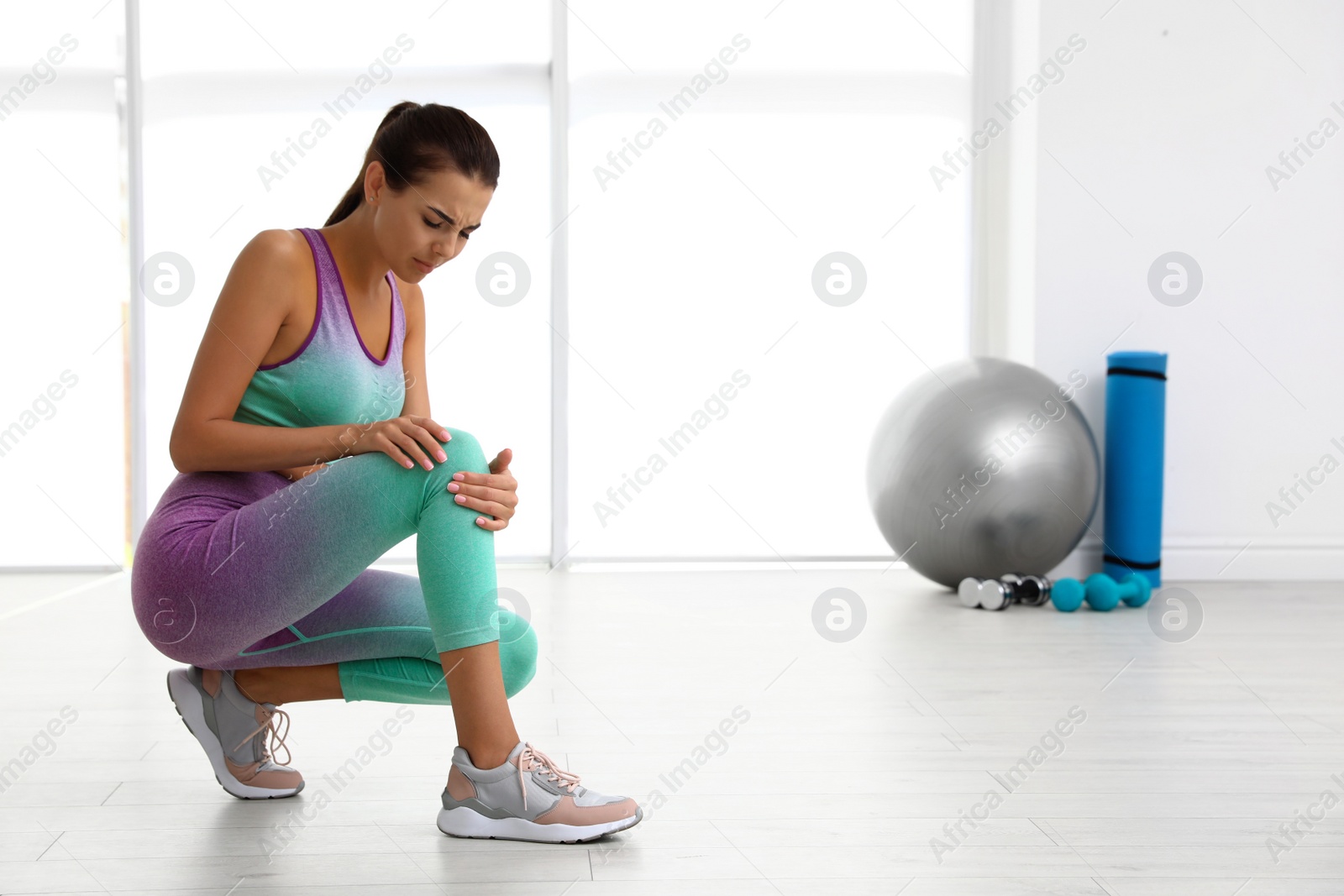 Photo of Young woman in sportswear having knee problems at gym. Space for text