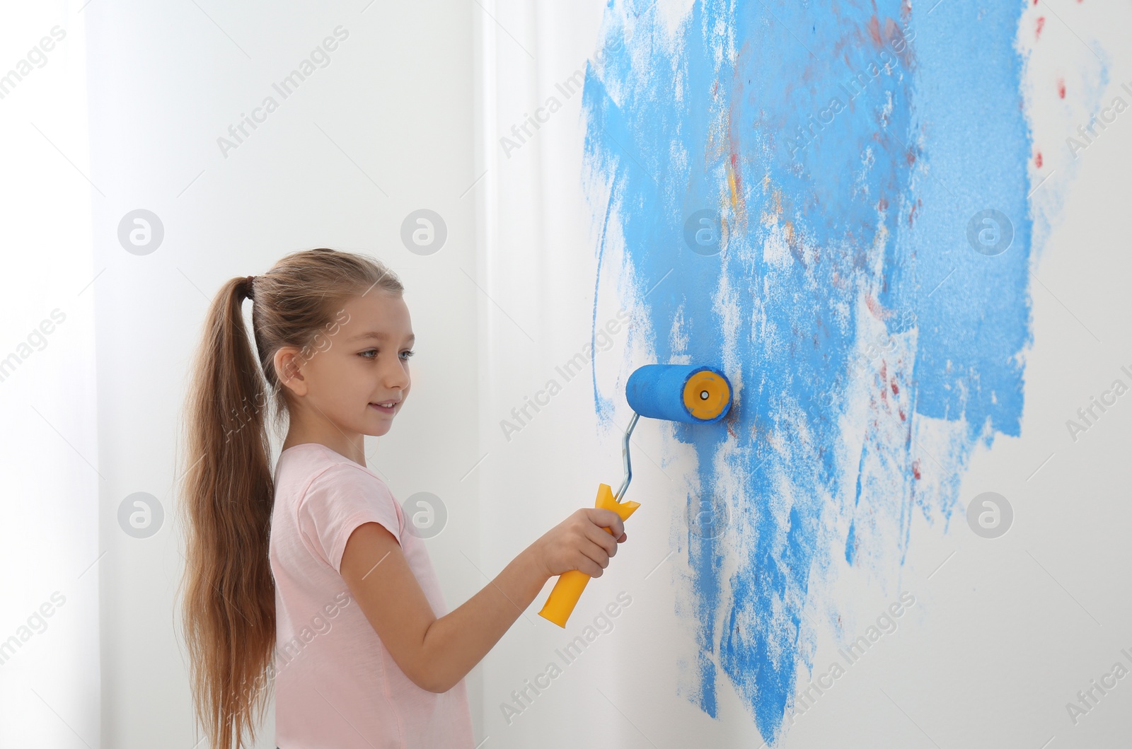 Photo of Little child painting wall with roller brush indoors