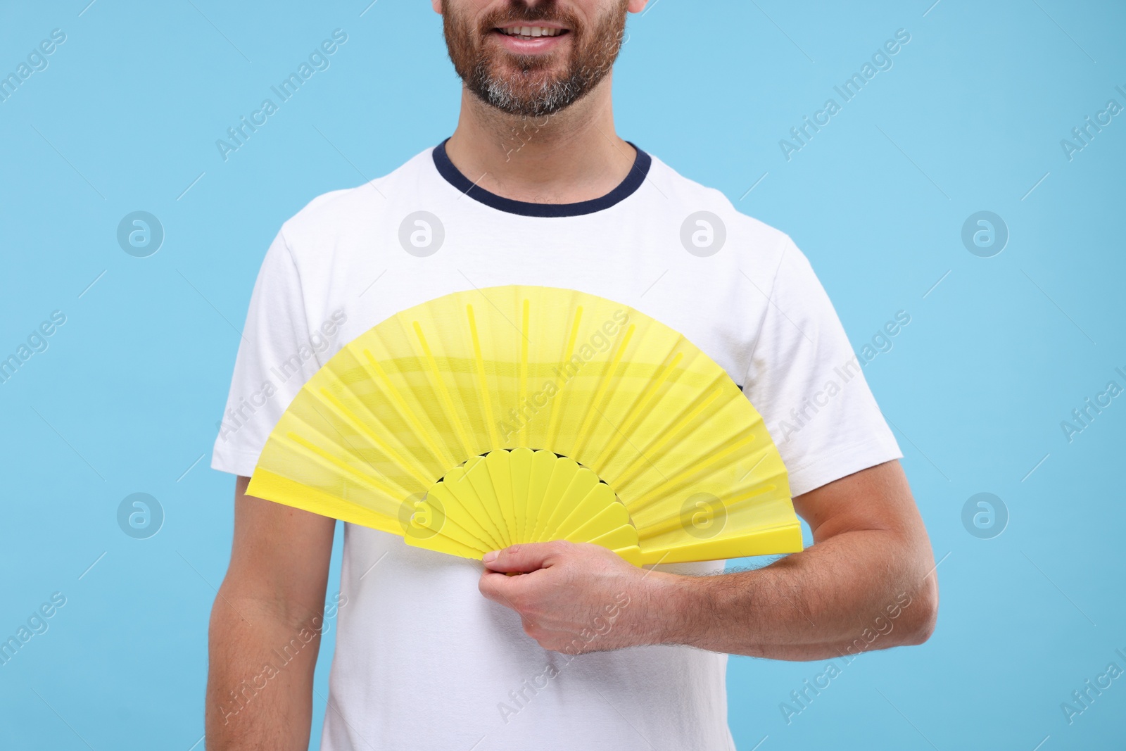 Photo of Man holding hand fan on light blue background, closeup