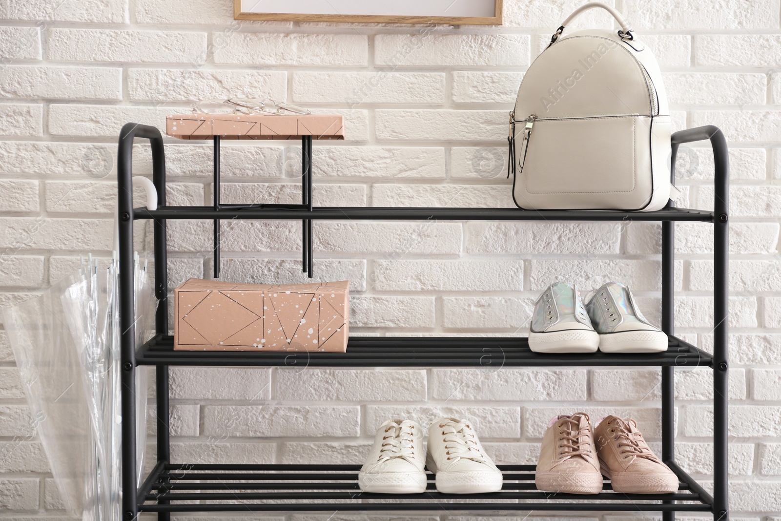 Photo of Shelving rack with stylish women's shoes and accessories near white brick wall indoors