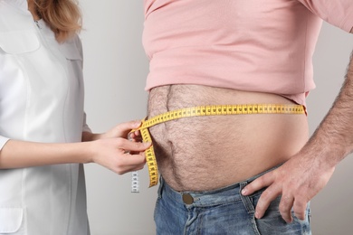 Photo of Doctor measuring overweight man's waist on color background, closeup