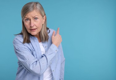 Surprised senior woman pointing at something on light blue background, space for text