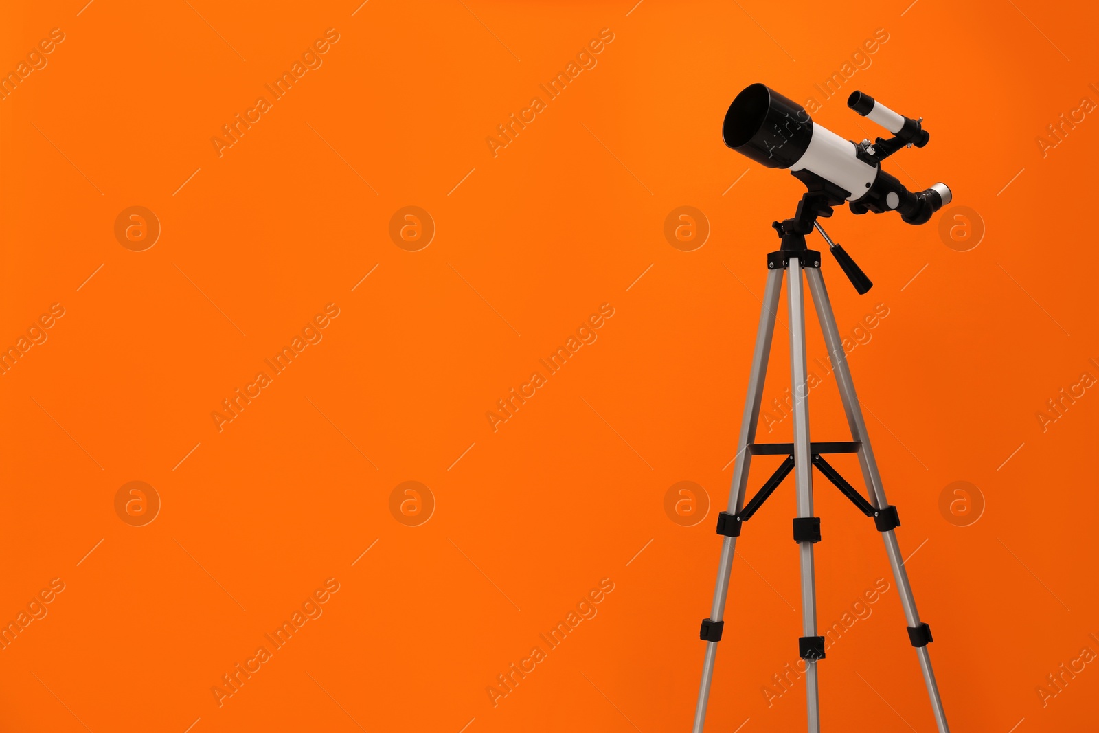 Photo of Tripod with modern telescope on orange background. Space for text